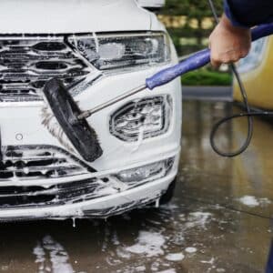Man cleaning his car using high pressure water. Young man washing his car in a self-service car wash station. Professional car detailing and cleaning services. Auto washing concept.