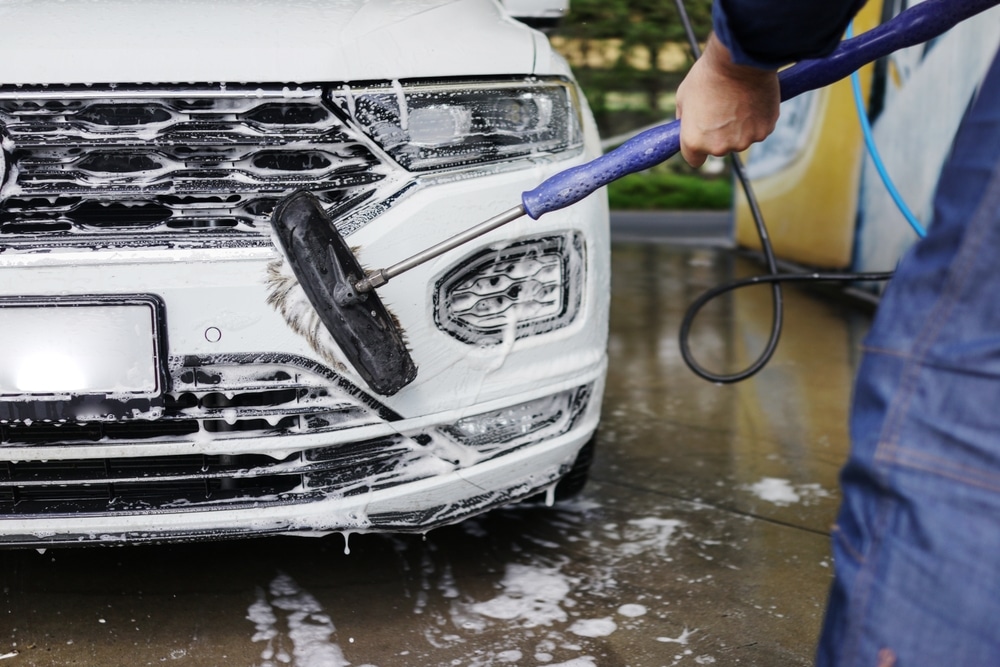 Man cleaning his car using high pressure water. Young man washing his car in a self-service car wash station. Professional car detailing and cleaning services. Auto washing concept.